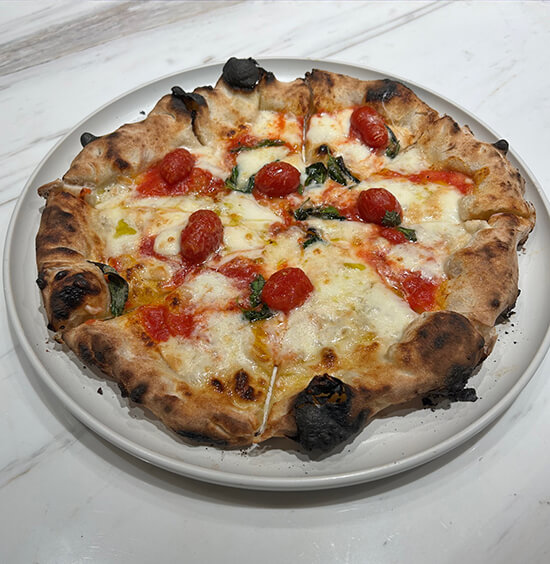 The signature Tamaki Pizza at Pizza Studio Tamaki — pecorino Romano, smoked mozzarella, basil, and roasted tomatoes.
